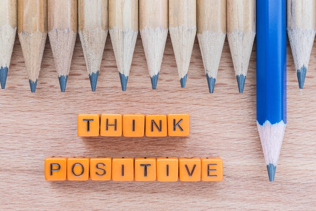 Words Think Positive on wooden table with group of pencils.