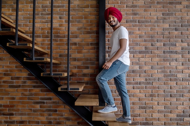 Work from home. Young indian man in red turban standing on stairs