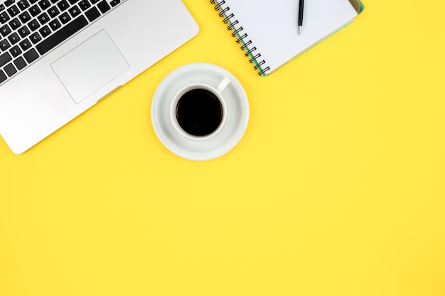 Work space layout with notepad laptop and coffee cup on a yellow background