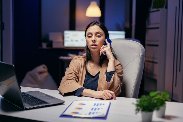 저녁에 전화로 고객과 이야기하는 워커홀릭 매니저. 전화 통화 중에 초과 근무를 하는 기업 비즈니스에서 밤늦게 일하는 여성 기업가.