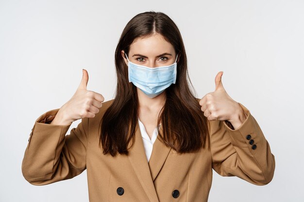 Workaplce and pandemic concept close up portrait of business woman showing thumbs up signs wearing m...