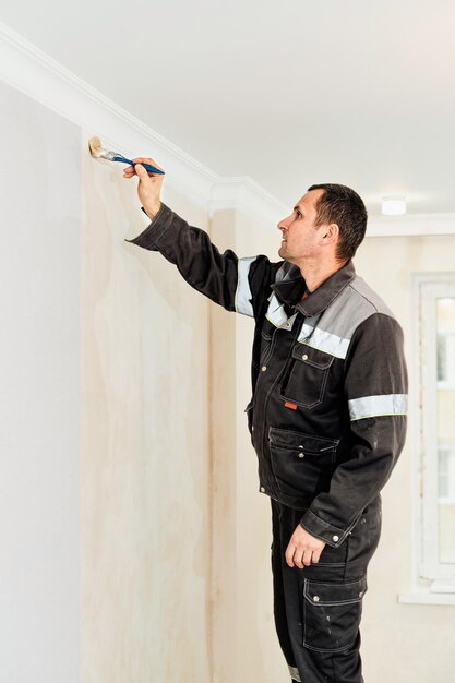 労働者は、壁紙を貼る前に壁に接着剤を塗布するか、壁にプライマーを塗布します選択的な焦点アパートの垂直フレームの改修と修復のアイデア