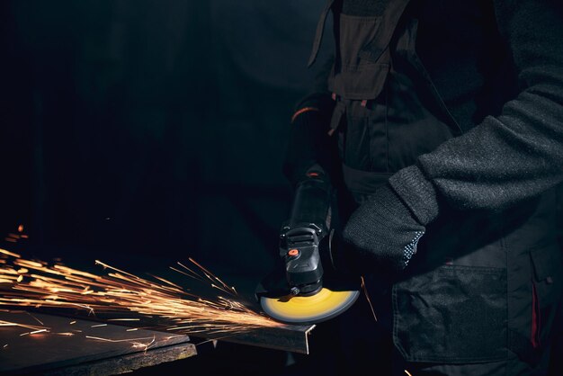 Рабочий в черных перчатках работает на угловой шлифовальной машине с металлом