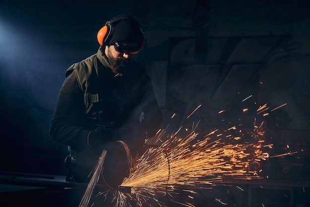 Worker in dark suit grinding on steel structure in modern