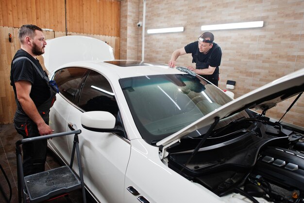 ガレージの詳細を説明する作業員が、ポリウレタン製の砂利防止フィルムカバーを白い高級車に取り付けました