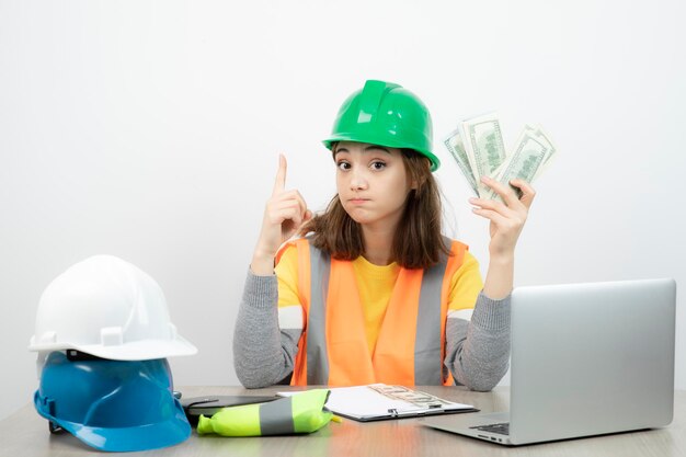 Worker female in orange vest and green helmet sitting at the desk . High quality photo