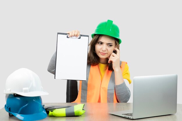 노트북과 클립보드가 있는 책상에 앉아 있는 제복을 입은 여성 노동자. 고품질 사진