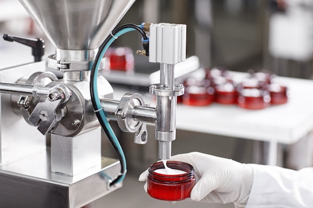 Worker filling container with cream in cosmetic factory