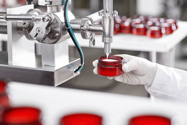 Worker filling container with cream in cosmetic factory