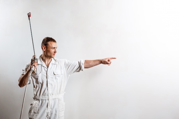 Worker holding spray gun on white wall.