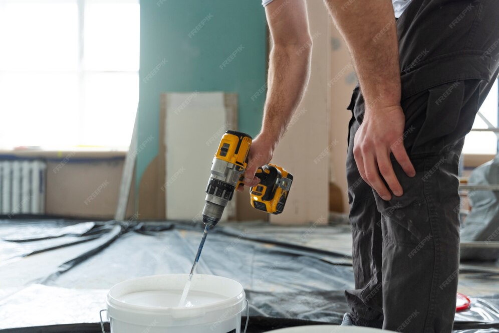 A worder mixing paint using a drill
