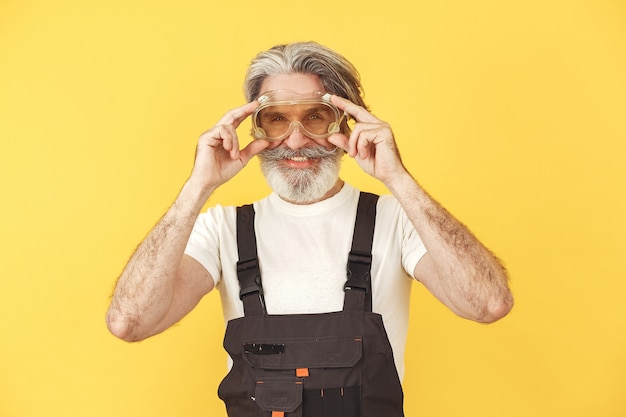 Worker in overalls. Man with tools. Senior in yellow glasses.