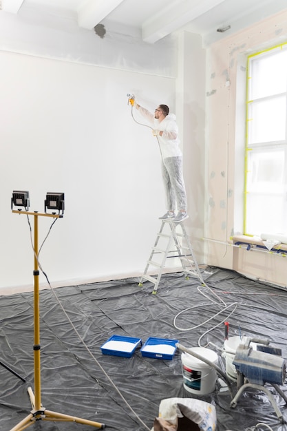 Worker painting wall on ladder full shot