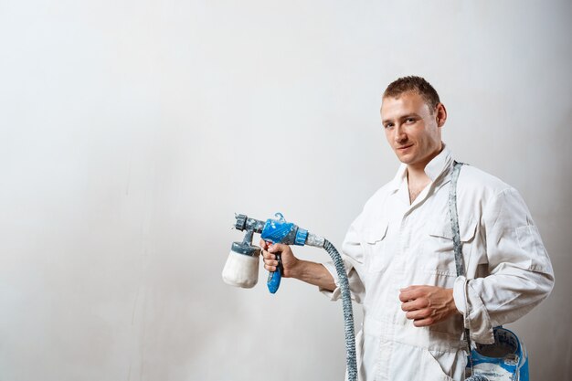 Worker painting wall with spray gun in white color