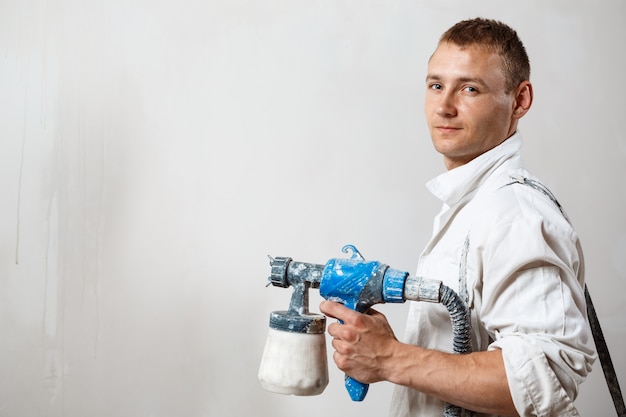 Worker painting wall with spray gun in white color