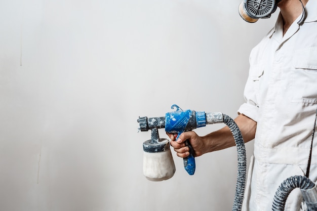 Worker painting wall with spray gun in white color.