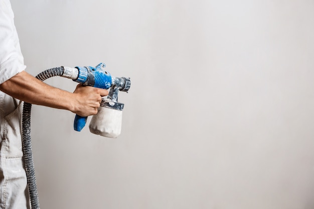 Worker painting wall with spray gun in white color.