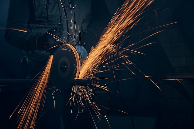 Worker polishing metal with special equipment in dark room