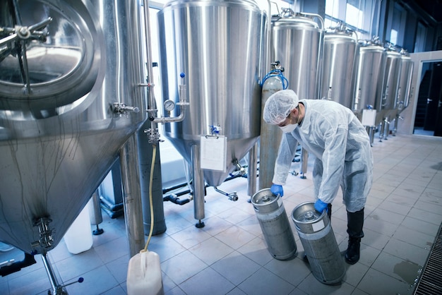 Worker in protective suit carrying chemicals in metal reservoirs