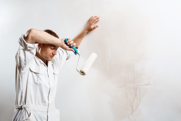 Worker resting, holding roller on white wall.