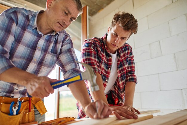 Worker sticking nail into wooden plank