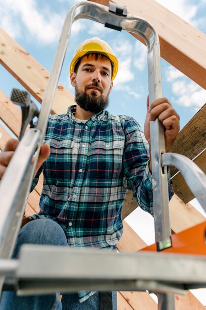 はしごを使って家の屋根を建てるヘルメットをかぶった労働者