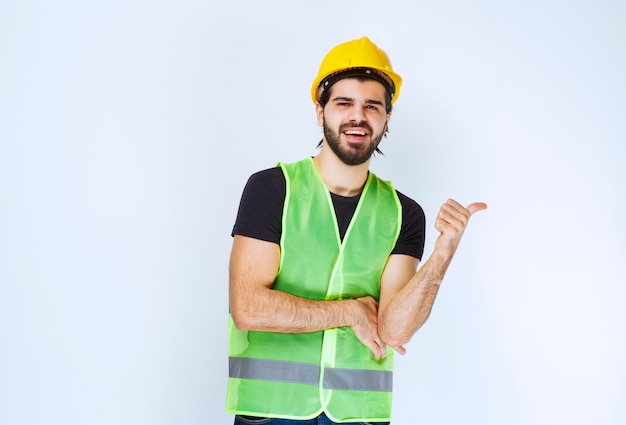 Worker in yellow helmet and gear pointing behind.