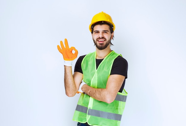 Worker in yellow helmet and workshop gloves showing enjoyment sign.