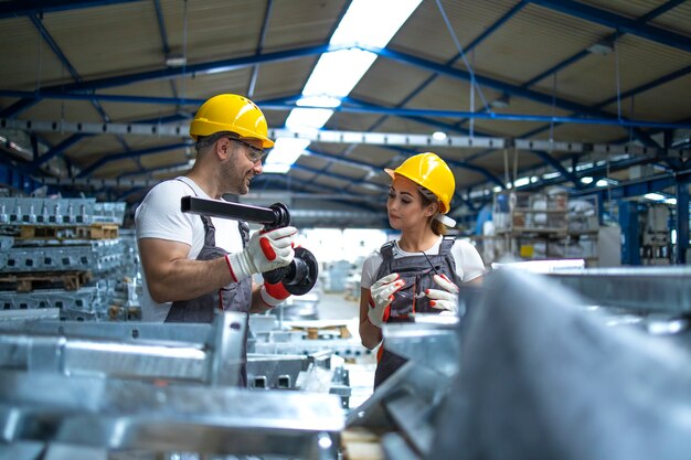 Workers checking quality of metal parts manufactured in factory