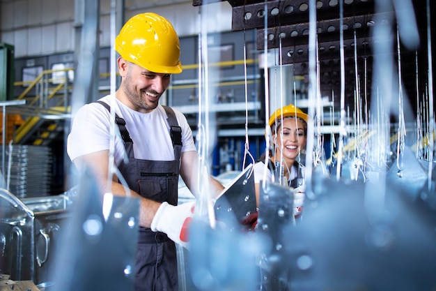 Workers in uniforms and yellow protective hardhats working in factory