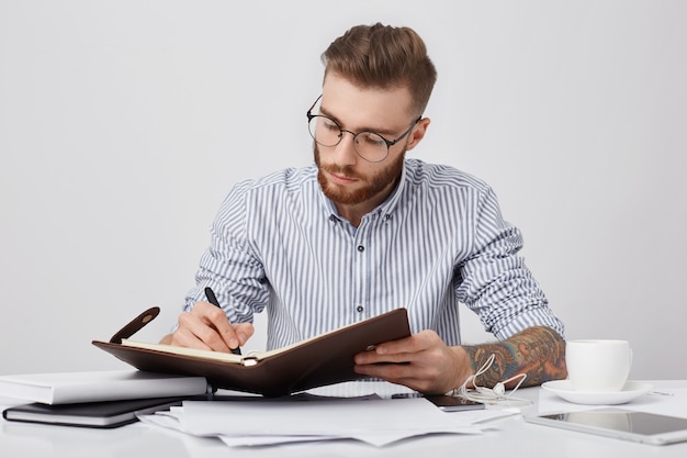 Бесплатное фото Рабочие моменты. сосредоточенный серьезный стильный татуированный мужчина в строгой рубашке и круглых очках