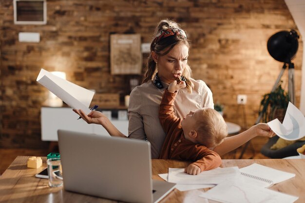 Working mother feeling stressed out while son is distracting her and feeding her with a cookie
