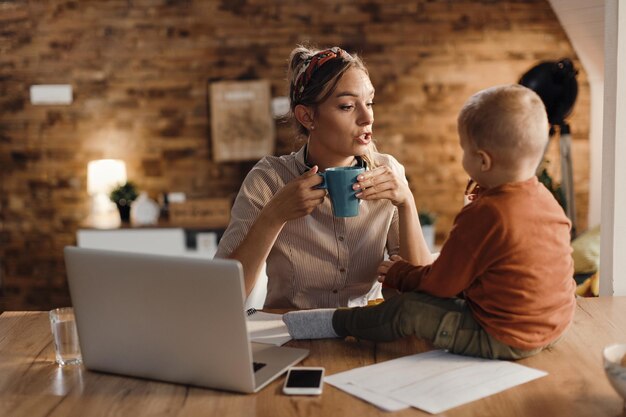 Working mother talking to her small son while having a cup of coffee at home