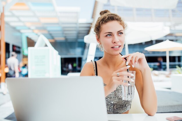 Working outdoors. Beautiful woman in funky hat working on laptop and smiling while sitting outdoors