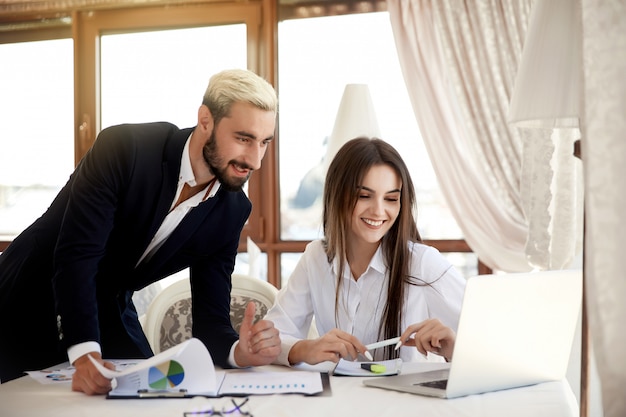 Working process in the business center of a young brunette woman and an attractive man inside the building looking at the laptop