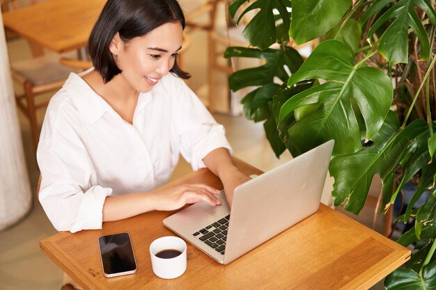 コーヒーを飲みながらレストランから離れてフリーランスで勉強しているラップトップを使用してカフェで働く女性