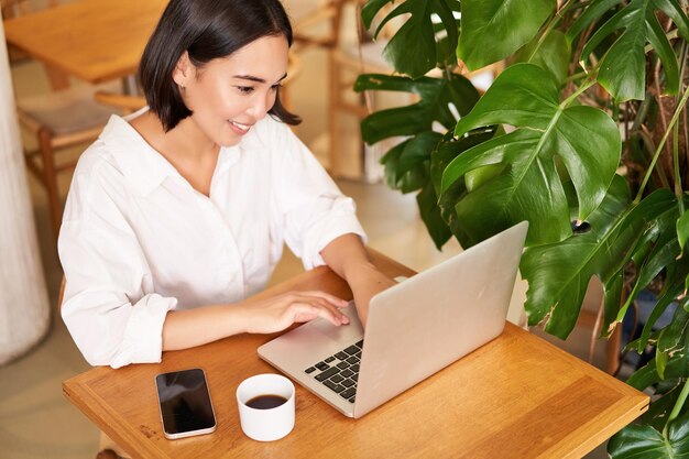 Working woman in cafe using laptop studying remotely freelancing from restaurant drinking coffee