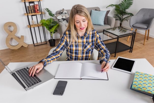 Working woman writing in notebook and working at laptop 