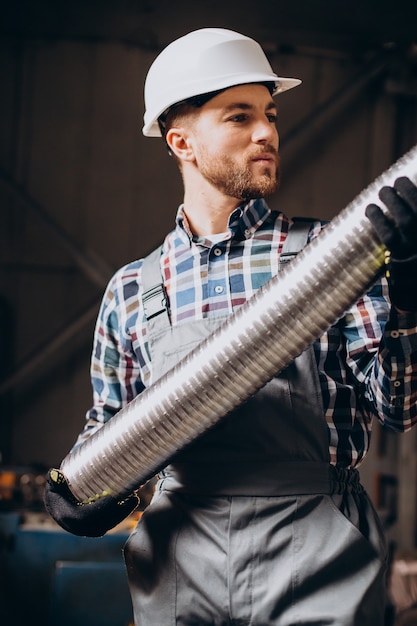 Foto gratuita operaio che indossa elmetto lavorando con tubo metallico in fabbrica