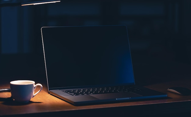 Workplace in the office with laptop and coffee in the dark room at night