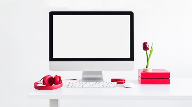 Workplace with keyboard near monitor, computer mouse, ornament flower and headphones