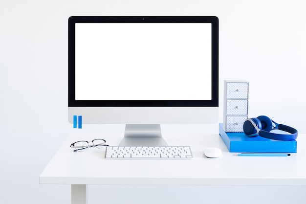 Workplace with keyboard near monitor, eyeglasses and headphones