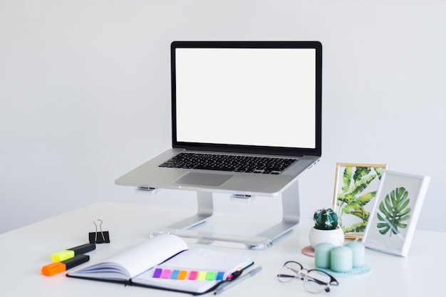 Workplace with laptop on stand near eyeglasses, notebook and photo frames