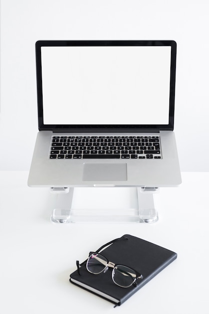 Workplace with laptop on stand near eyeglasses and notepad