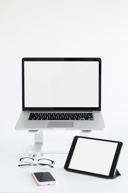 Workplace with laptop on stand near eyeglasses, tablet and mobile phone