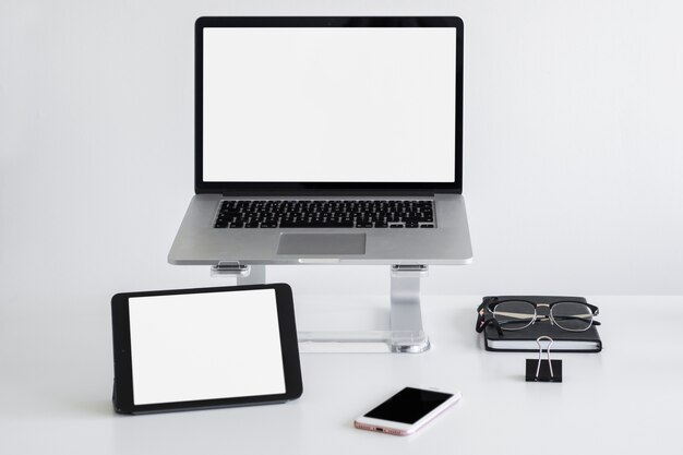 Workplace with laptop on stand near eyeglasses, tablet and smartphone