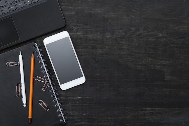 Workplace with smartphone, notebook, on black table. Top view