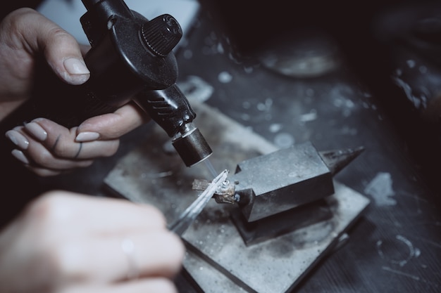 In the workshop, a woman jeweler is busy soldering jewelry