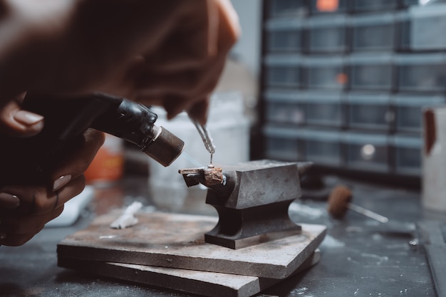 In the workshop, a woman jeweler is busy soldering jewelry