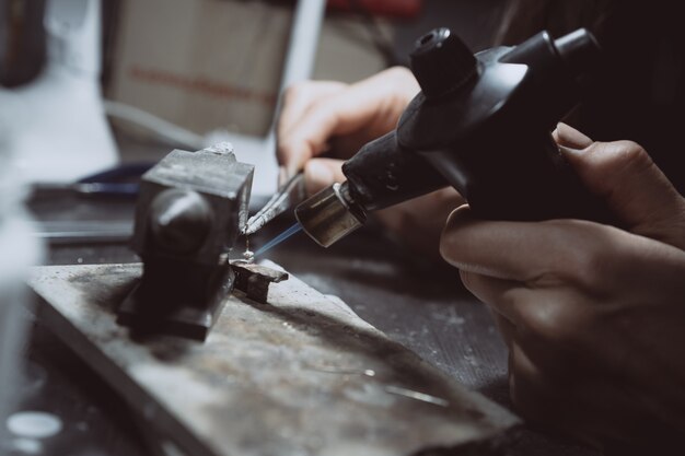 In the workshop, a woman jeweler is busy soldering jewelry